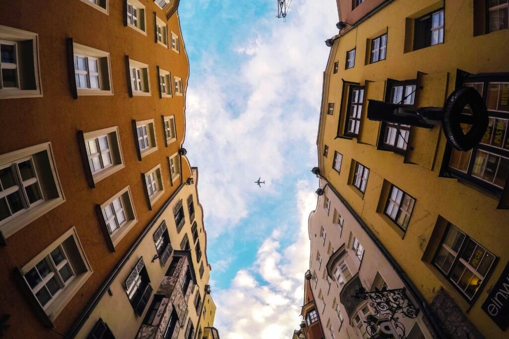 Dois condomínios de frente para o outro vistos de baixo com o céu azul com nuvens por cima para ilustrar texto sobre os dois lados de morar em condomínio.